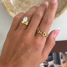 Hand wearing a gold ring with a blurred indoor background