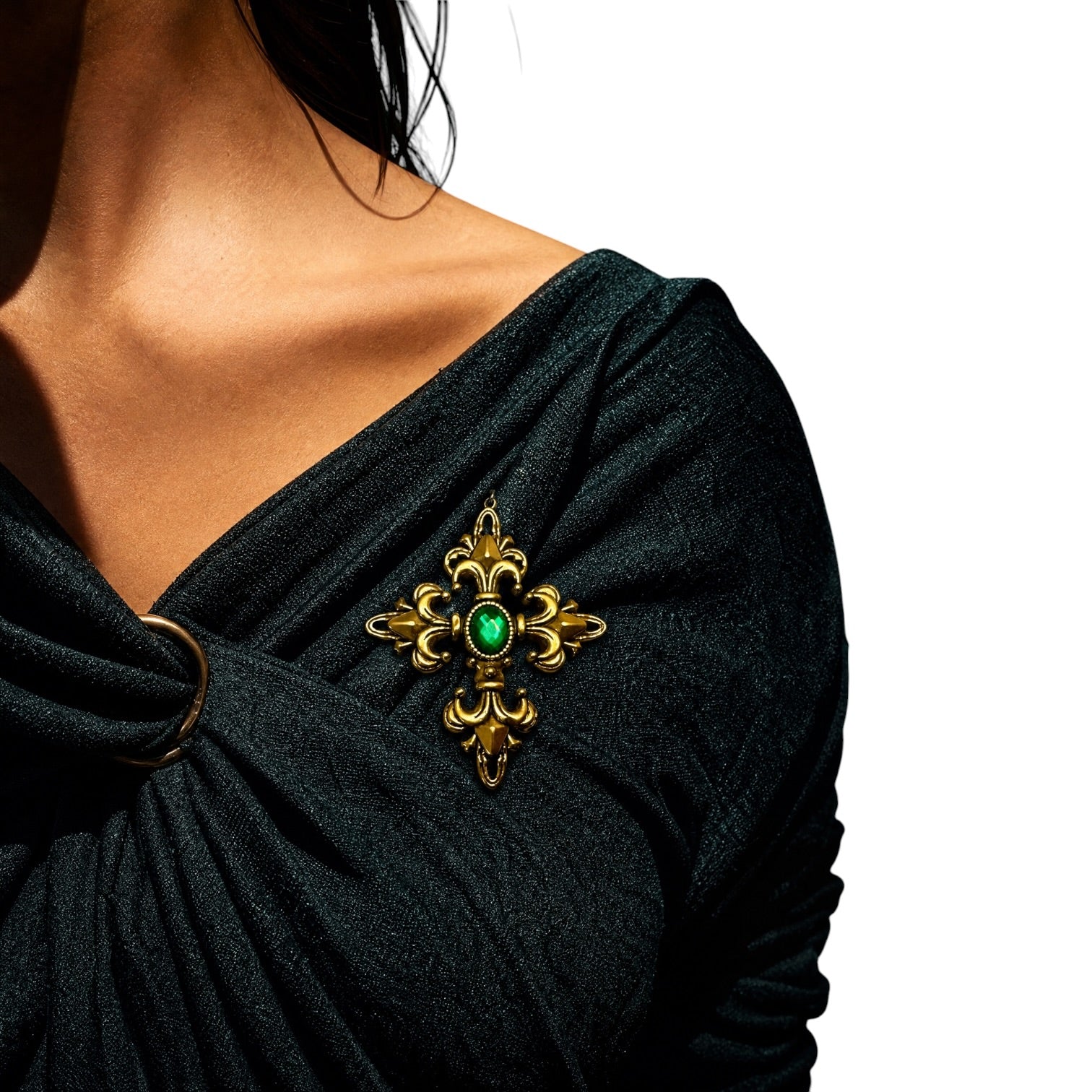 A close-up of a woman wearing a black draped top and wearing a gold brooch with a green oval center stone on her shoulder.