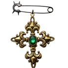 A vintage-style safety pin brooch featuring an ornate gold-toned cross pendant with a faceted green gemstone at the center, set against a plain white background.