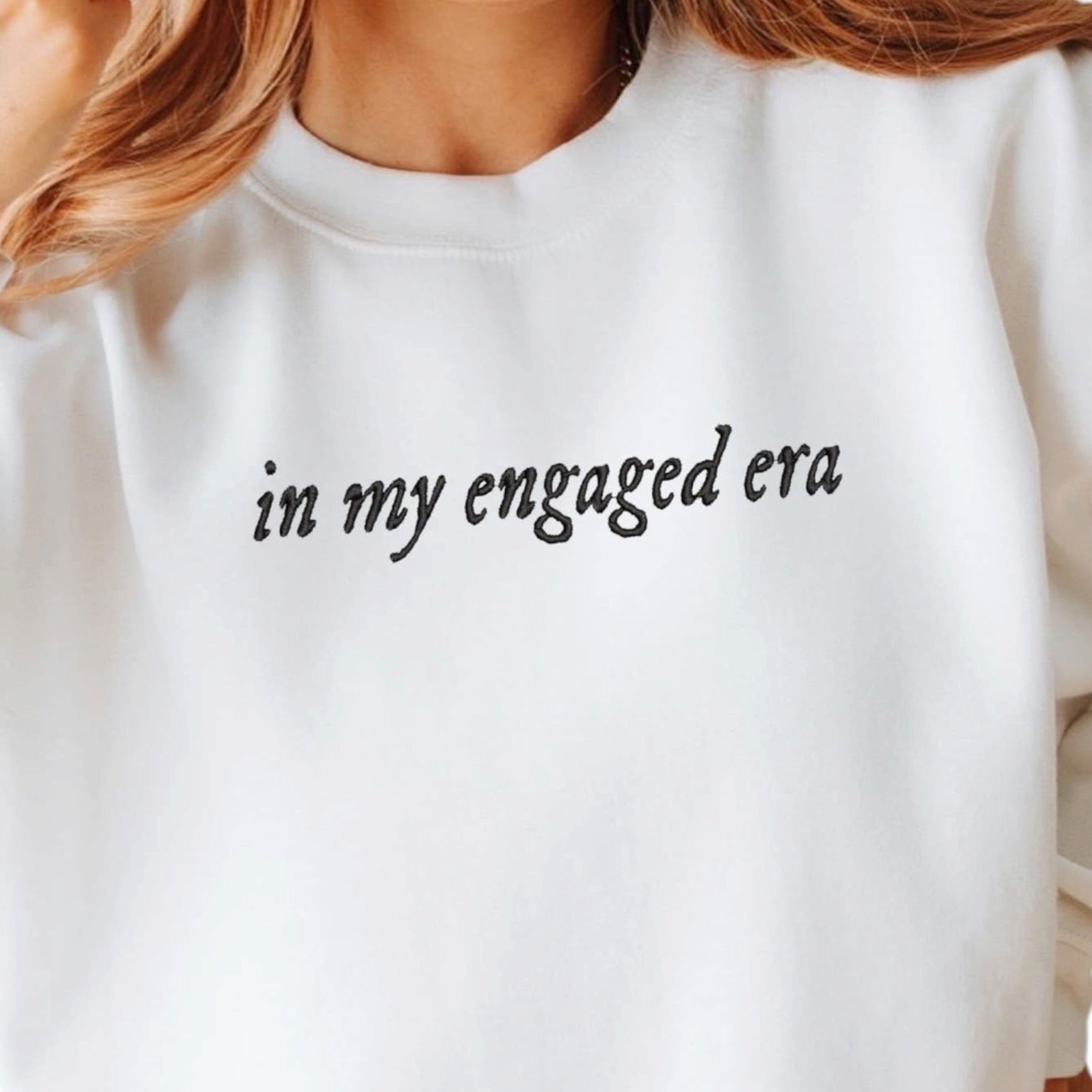 White sweatshirt with text 'in my engaged era' on a plain background