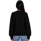 A woman viewed from the back wearing a black knit sweater and light blue jeans against a plain white background.