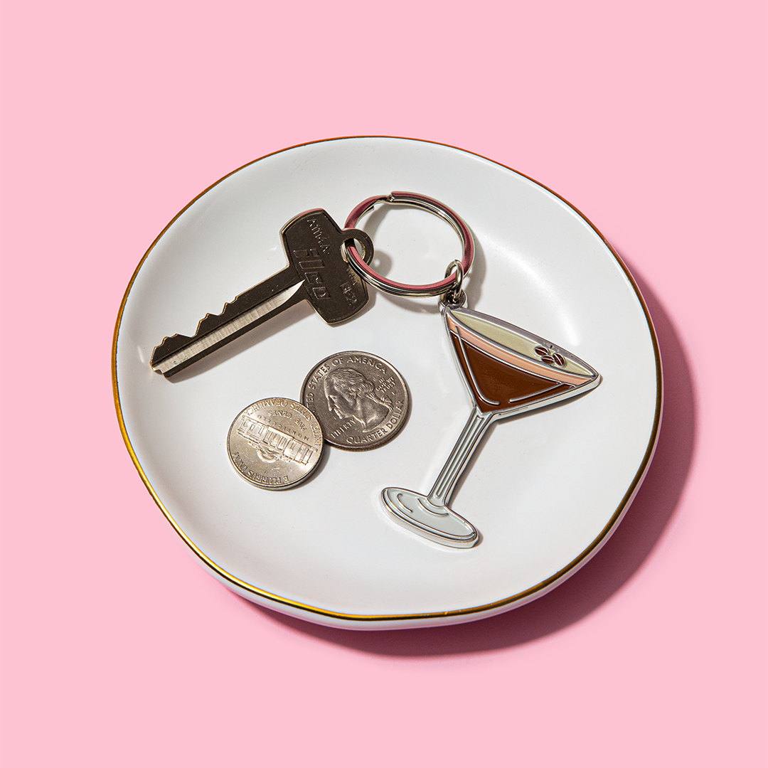 Trinket dish with key, coins, and martini glass charm on a pink background