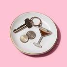 Trinket dish with key, coins, and martini glass charm on a pink background