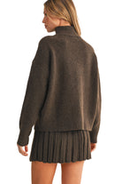 Woman wearing a brown sweater and pleated skirt on a beige background