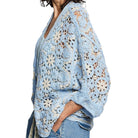 Woman wearing a light blue floral crochet shrug on a white background