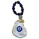A beaded necklace featuring a large white shell pendant with a blue and white evil eye design, accented by a light green bead and dark blue round beads.