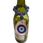 A green glass bottle decorated with a blue beaded bracelet and a large evil eye glass charm, shown against a plain white background.