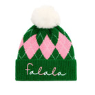 A green and pink argyle knit beanie with a fluffy white pom-pom on top and the word 'falala' embroidered in white script on the green cuff.