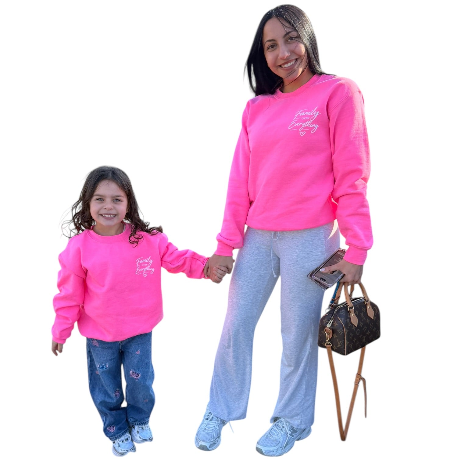 Woman and child wearing matching pink sweatshirts with a logo, standing next to a handbag on a white background.