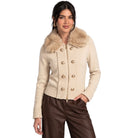 A woman modeling a cropped beige knit cardigan with a large faux-fur collar and gold-tone buttons, paired with dark brown pants, against a plain white background.