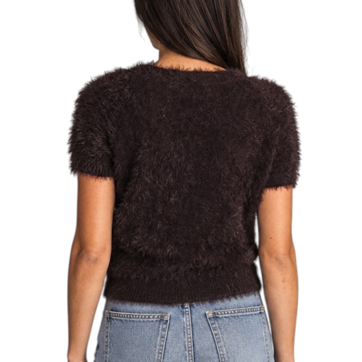 A woman viewed from the back wearing a short-sleeve, fuzzy knit top in dark brown, paired with light blue jeans, against a plain white background.