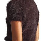 Close-up of a person wearing a dark brown fuzzy short-sleeve top or vest against a plain white background.