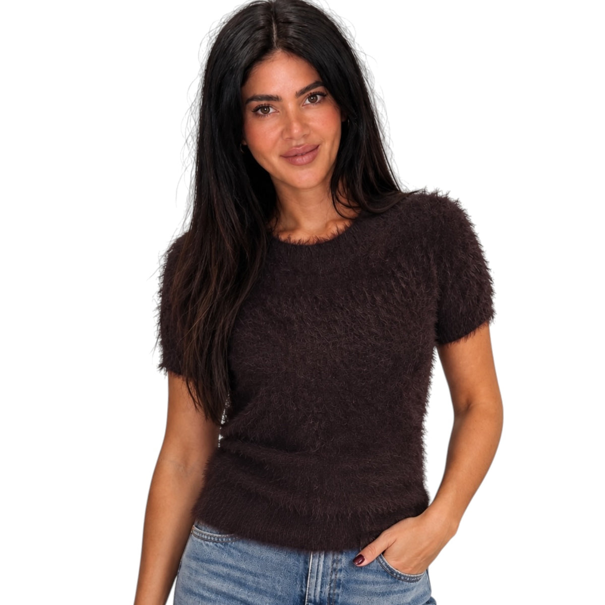 A woman with long dark hair wearing a short-sleeve, fuzzy dark brown knit sweater and blue jeans, photographed against a solid white background.