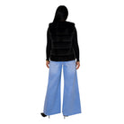 A woman shown from the back wearing a black faux-fur vest over a black long-sleeve top and light blue wide-leg jeans, against a plain white background.