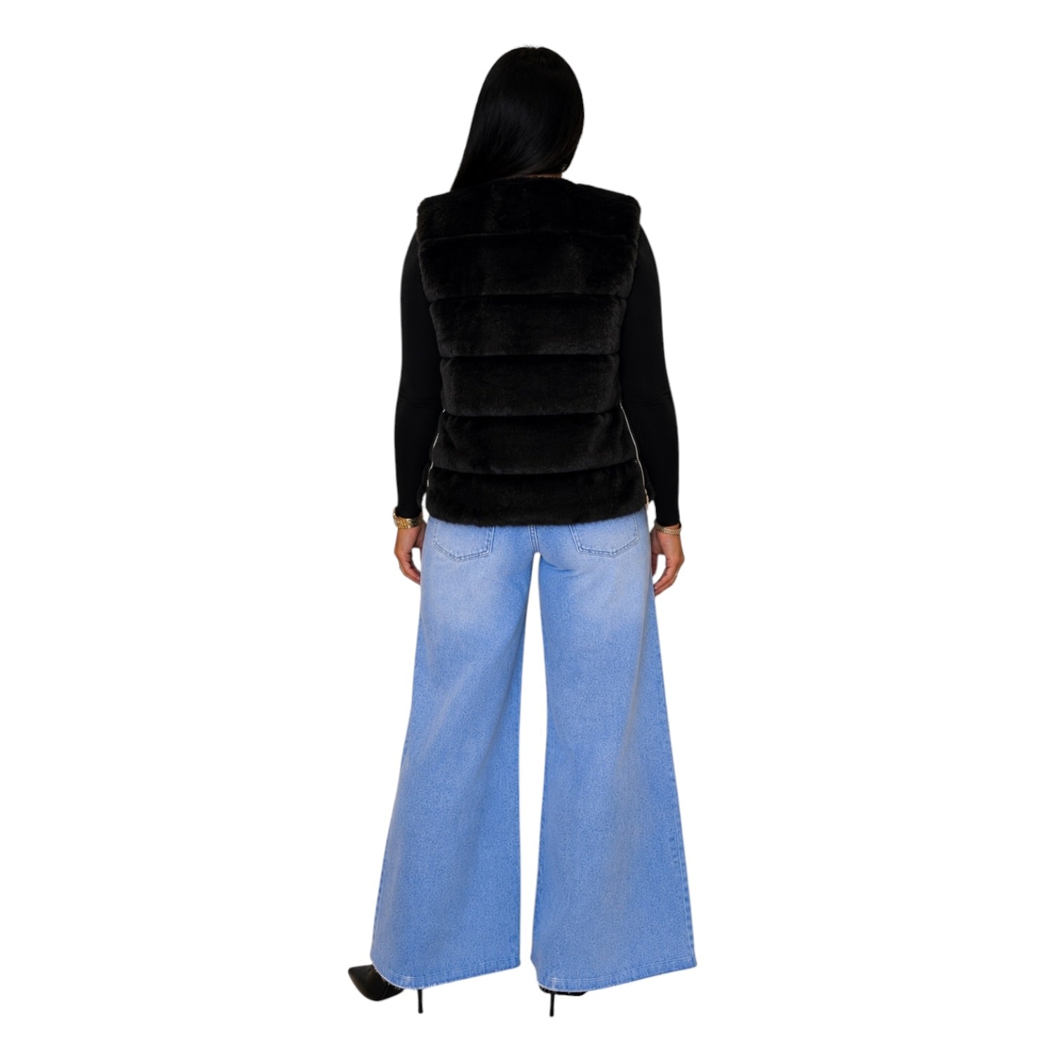 A woman shown from the back wearing a black faux-fur vest over a black long-sleeve top and light blue wide-leg jeans, against a plain white background.