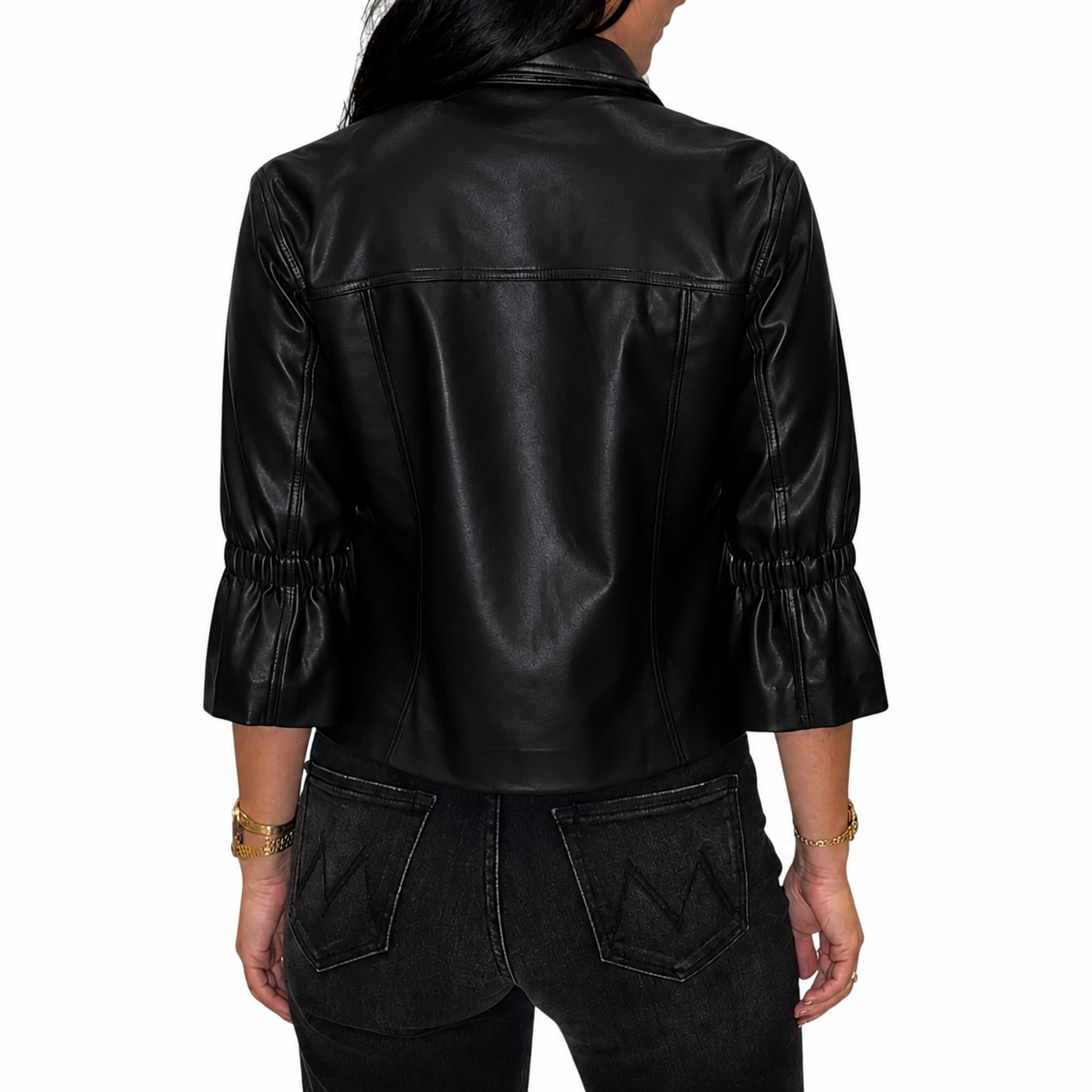 A woman viewed from the back wearing a black faux-leather jacket with gathered three-quarter sleeves and dark jeans, against a plain white background.