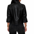 A woman viewed from the back wearing a black faux-leather jacket with gathered three-quarter sleeves and dark jeans, against a plain white background.