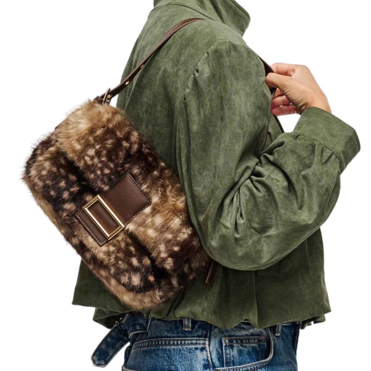 A person wearing an olive green jacket and blue jeans carries a brown and beige faux fur shoulder bag with a brown leather strap and gold-tone buckle against a white background.