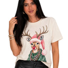 A woman wearing a cream-colored t-shirt with a festive graphic of a reindeer wearing a pink Santa hat, green sweater, and red nose. The background is solid white.