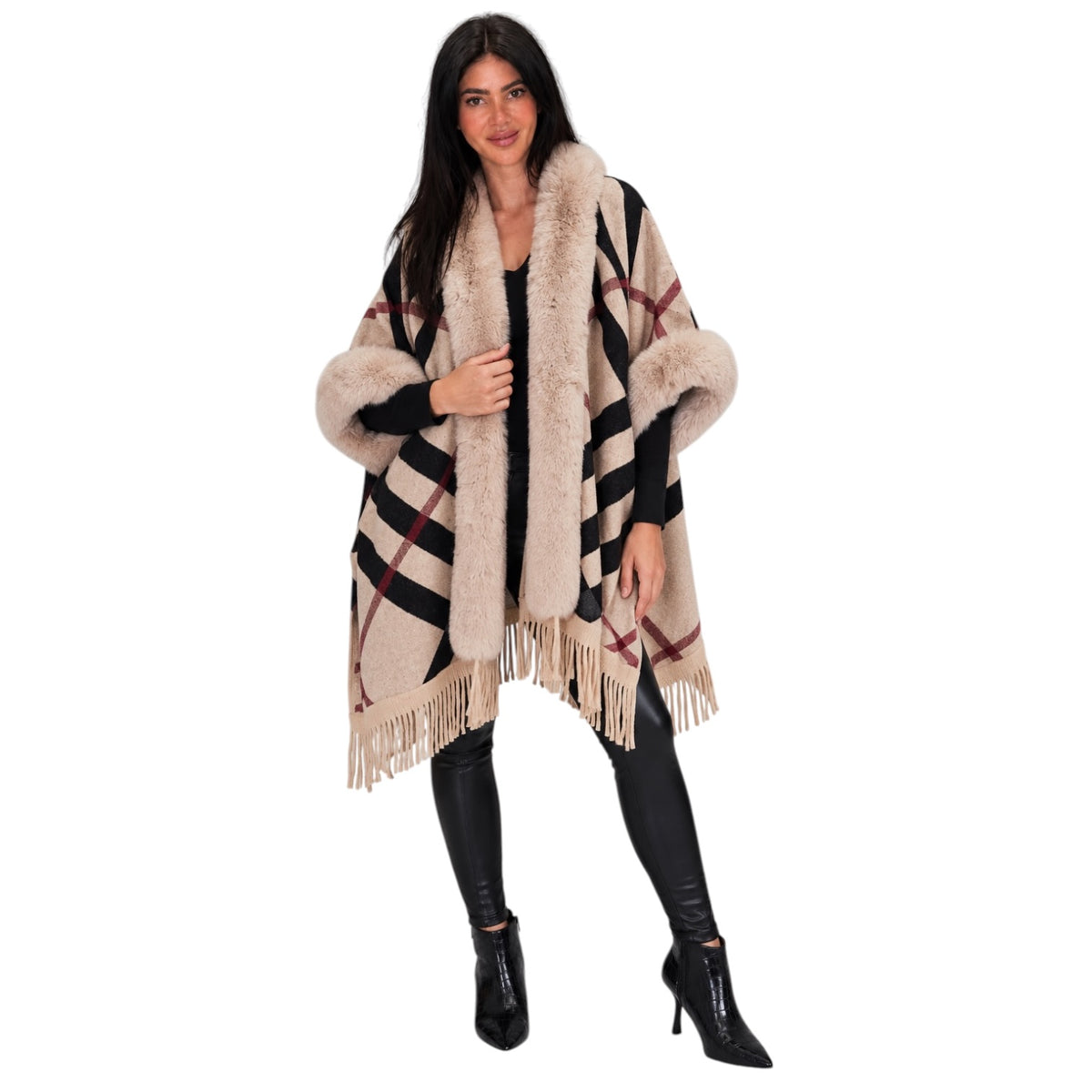 A woman modeling a beige faux fur-trimmed plaid poncho with fringe, worn over a black outfit on a solid white background.
