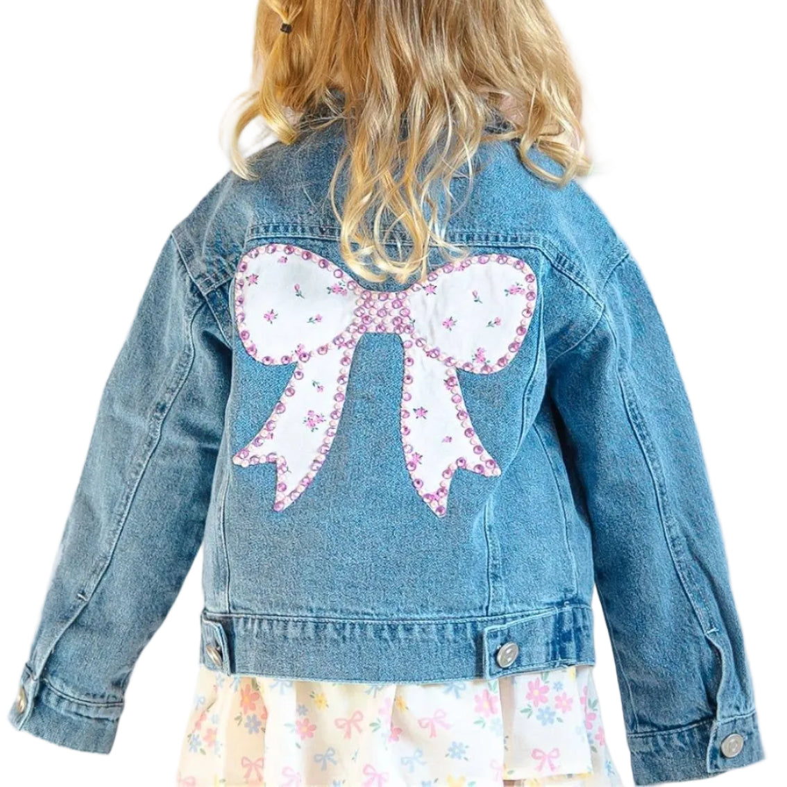 Child wearing a denim jacket with a large pink bow on the back, standing against a light pink background.