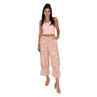 A woman modeling a two-piece outfit consisting of a light pink sleeveless crop top and high-waisted, wide-leg floral pants with lace ruffle hems, set against a plain white background.