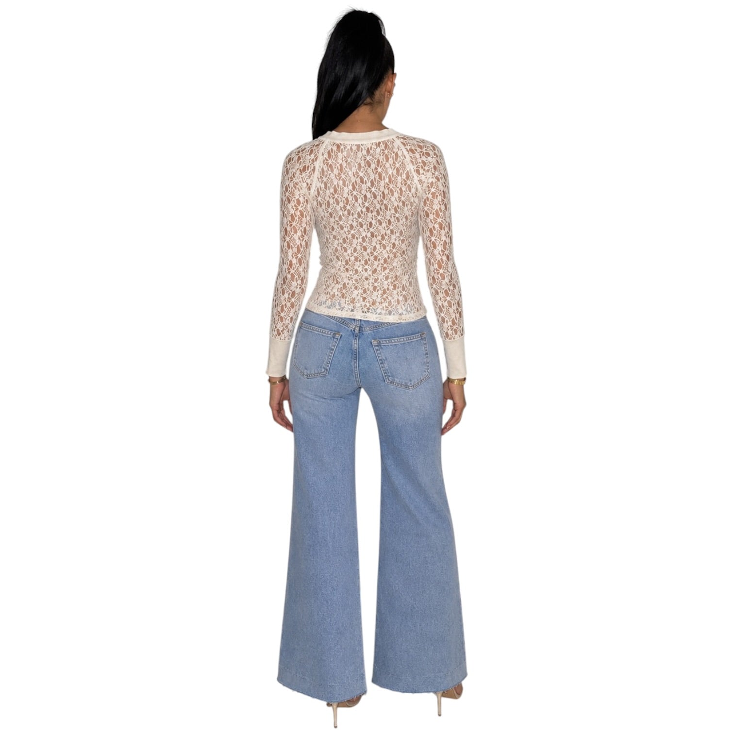 A woman shown from the back wearing a beige lace long-sleeve crop top and light blue wide-leg jeans against a plain white background.