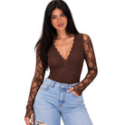 A woman modeling a brown lace long-sleeve bodysuit with a scalloped V-neckline, paired with light-wash blue jeans, against a plain white background.