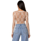 A woman shown from the back wearing a sheer beige lace long-sleeve crop top over light blue jeans, against a plain white background.