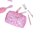 Pink cosmetic bag with floral design on a light pink surface with various beauty items.