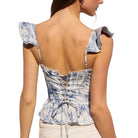 Woman wearing a blue and white patterned top with ruffled straps on a white background