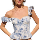 Woman wearing a blue and white patterned top with ruffled shoulders on a white background