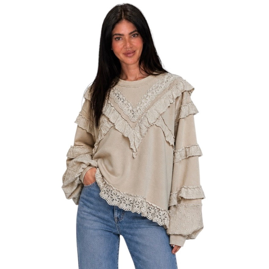 A woman modeling a beige long-sleeve top with layered ruffles and lace trim, paired with blue jeans, against a plain white background.