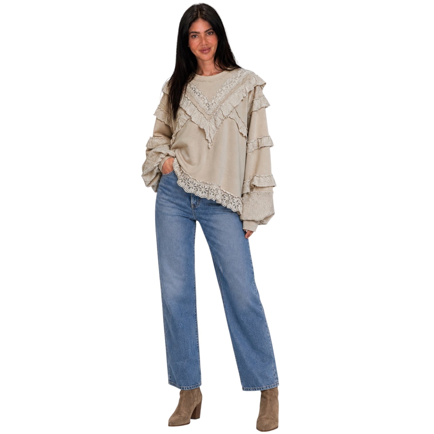 A woman modeling a beige long-sleeve blouse with layered ruffles and lace trim, paired with blue jeans and brown ankle boots, against a plain white background.