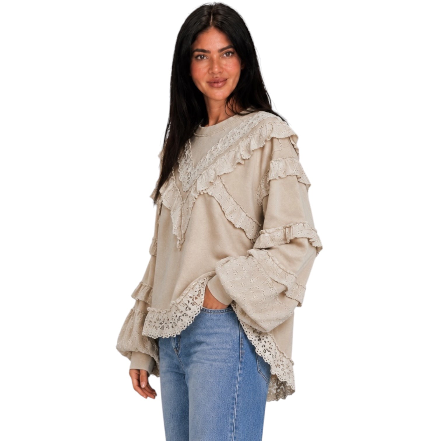 A woman modeling a beige long-sleeve top with layered ruffles and lace trim, paired with blue jeans, against a plain white background.
