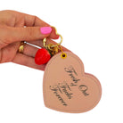 Heart-shaped keychain with strawberry charm and text held by a hand on a white background