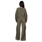 A woman viewed from the back wearing an olive green matching lounge set with long fringe detailing on the sleeves and pants, set against a plain white background.