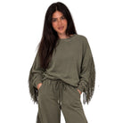 A woman modeling an olive green lounge set featuring a long-sleeve sweatshirt with fringe detailing on the sleeves and matching drawstring sweatpants, set against a plain white background.