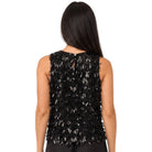 A woman viewed from the back wearing a sleeveless black embellished top with layered feather-like texture and black pants, against a plain white background.