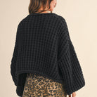 Person wearing a black chunky knit sweater on a beige background