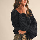 Woman wearing a black chunky knit cardigan on a beige background