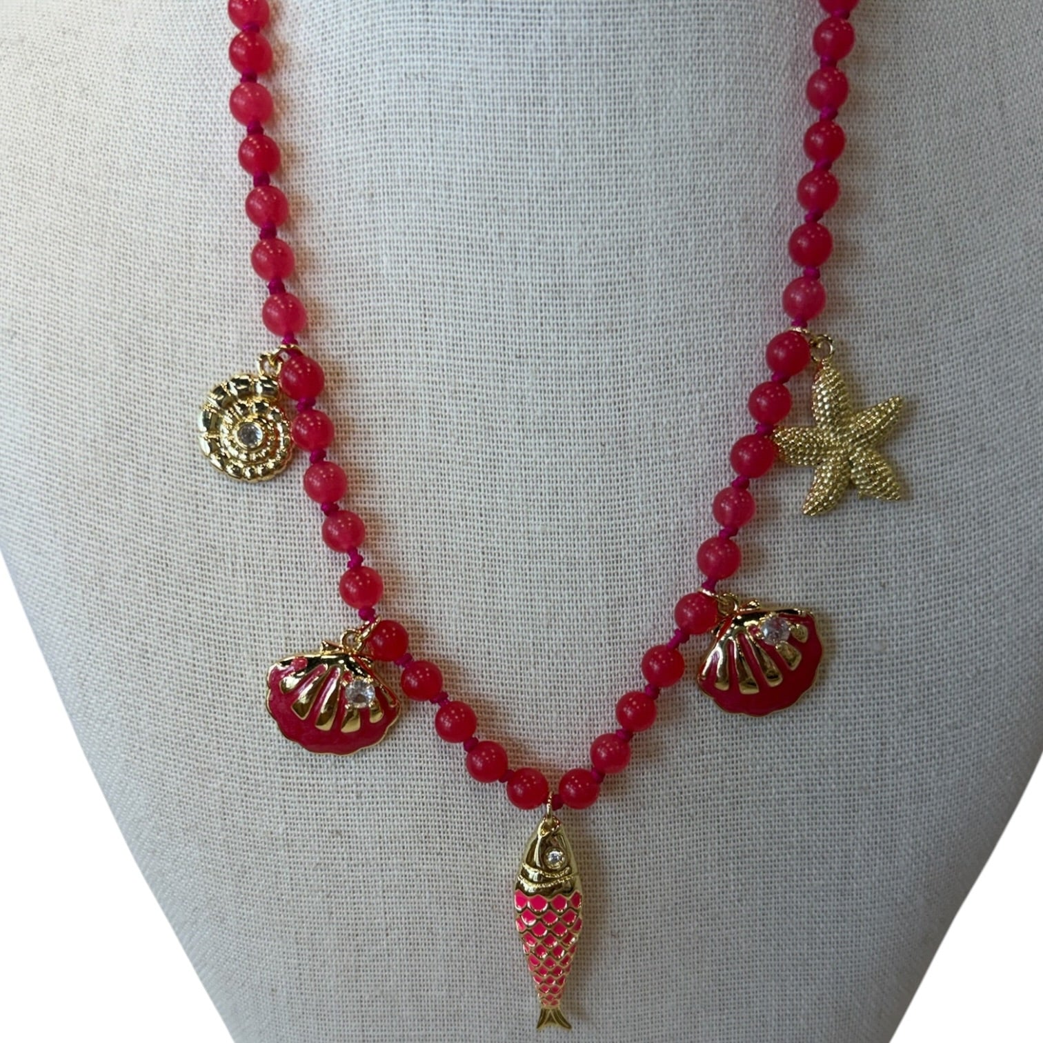 A red beaded necklace with gold-toned shell and starfish charms, displayed on a neutral fabric mannequin bust.