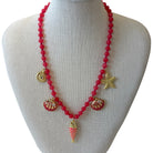 A red beaded necklace with gold-toned seashell, starfish, and fish charms, displayed on a light gray fabric mannequin bust.