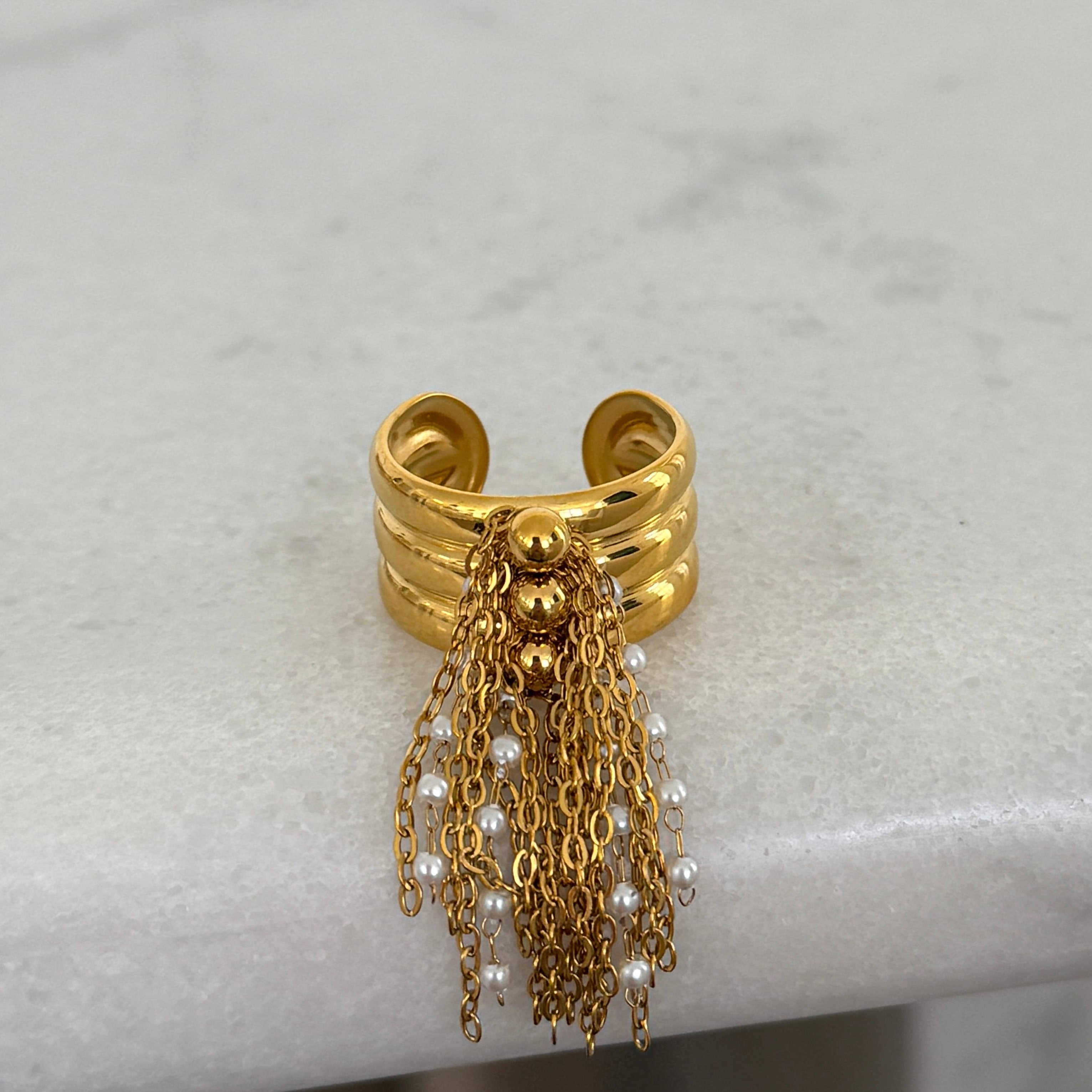 Gold ring with chains and pearls on a light gray background