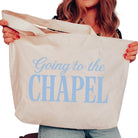 Person holding a tote bag with 'Going to the Chapel' text in blue.