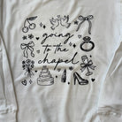 White shirt with black graphic design featuring wedding-related icons and text 'going to the chapel'.