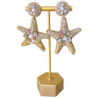 Starfish-shaped earrings on a gold stand with a white background