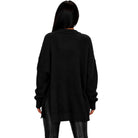 A woman viewed from the back wearing an oversized black textured knit sweater and black pants against a plain white background.