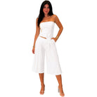 Woman wearing a white strapless top and wide-leg pants on a white background