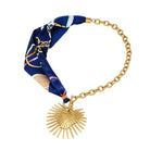 Necklace with a blue patterned fabric wrap and gold chain and heart sunburst charm on a white background